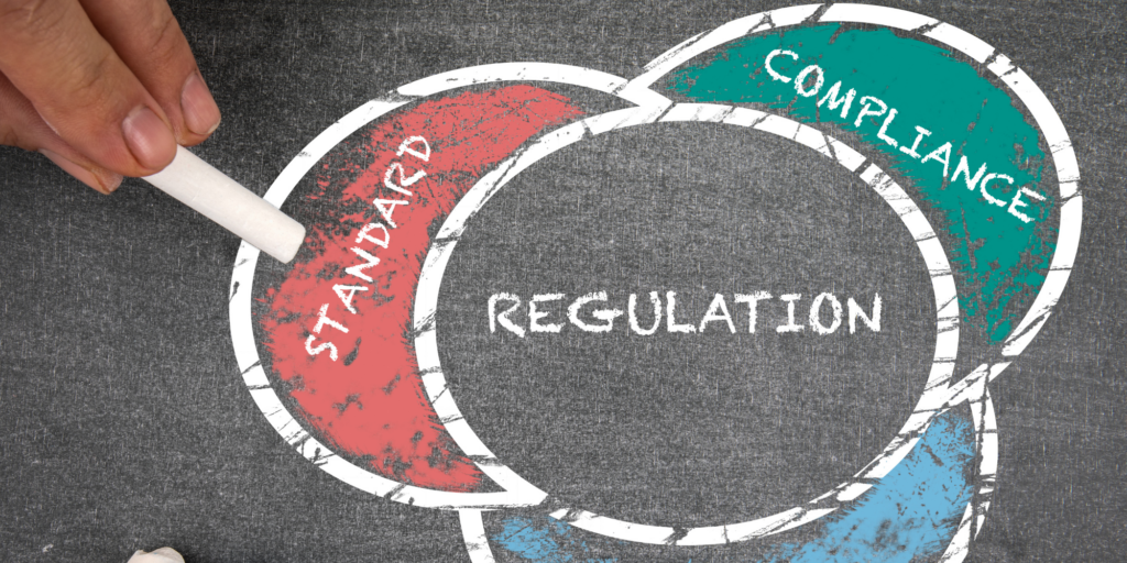 Image of a Venn diagram drawn with chalk with the words "regulation," "standard," and "compliance" inside each bubble.